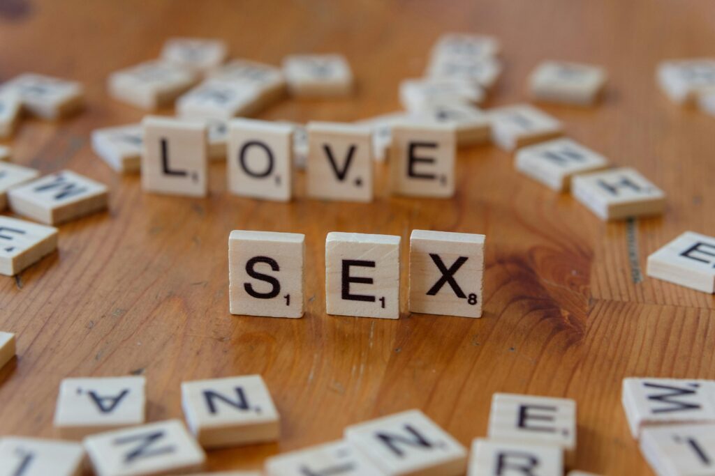 Scrabble tiles spelling 'Love' and 'Sex' on a wooden table, symbolizing relationships.
